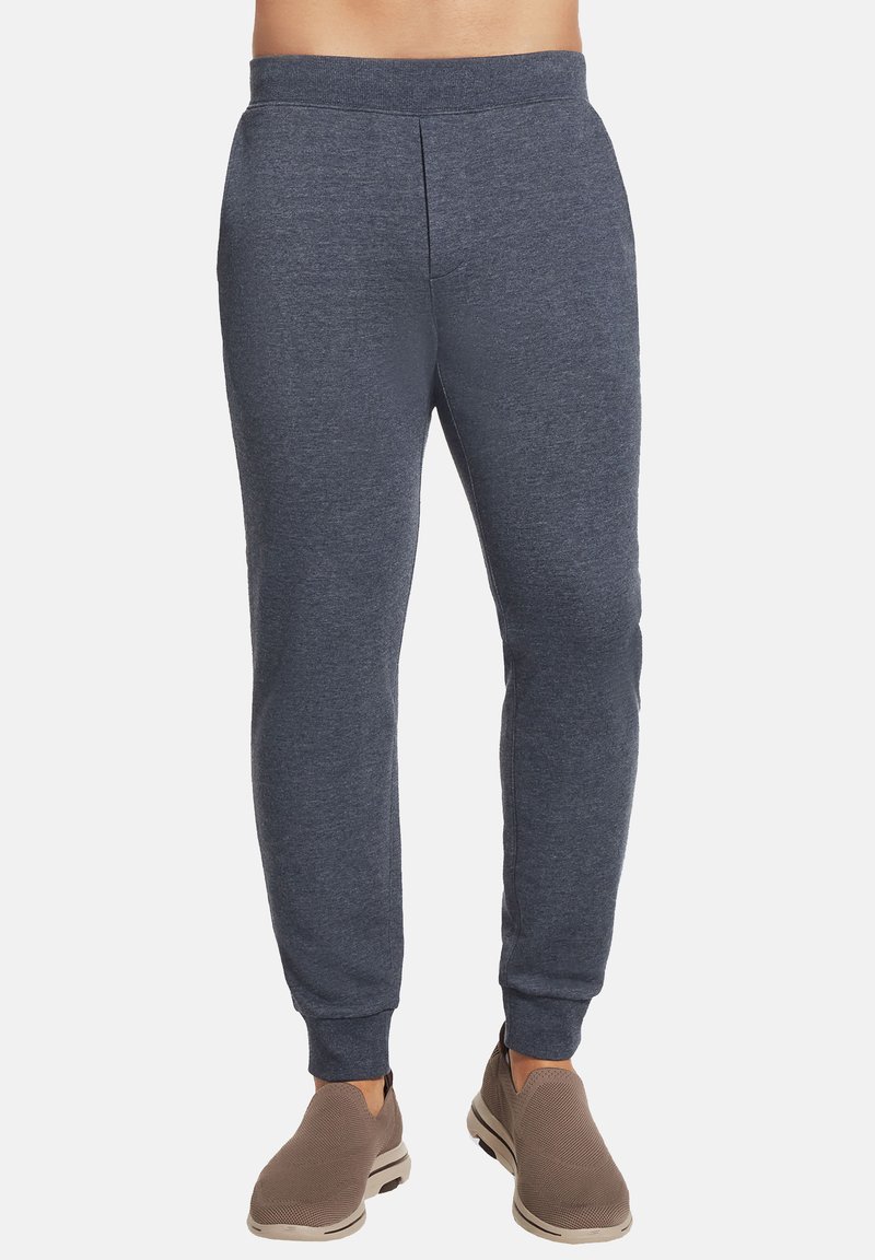 Pantalones jogger navy hechos de una tela suave, con un diseño entallado, cintura elástica y puños acanalados. Combinados con zapatos de slip-on marrón claro.
