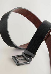 Gürtel mit einer schwarzen strukturierten Oberfläche und einer metallischen Schnalle, sowie einer glatten braunen Rückseite, die ein Zweifarbendesign betont.