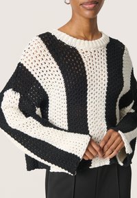 Knitinys megztinis su juodais ir grietinėlės spalvos pakaitiniais dryžiais, laisvas kirpimas, plačios rankovės ir apvali iškirptė. Tekstūruotas atviras mezgimo raštas.
