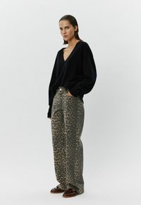 Pārsvarā liels melns V-veida džemperis apvienots ar augsto vidukli un platu kāju leopardu drukas biksēm. Izskatu papildina brūni mokasīni.