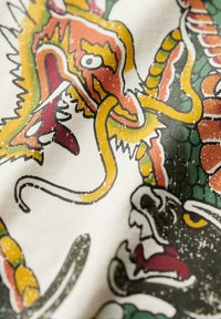 Tissu graphique mettant en avant un design de dragon détaillé avec des couleurs vibrantes : orange, vert et noir, ornés de contours texturés et de motifs complexes.