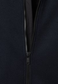 Marineblaue zipfelige Jacke mit strukturiertem Rippstoff, schwarzem Reißverschluss und glatter Innenschicht.