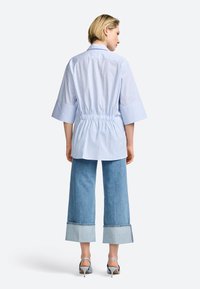 Chemise rayée bleu clair avec une taille cintrée et des manches larges, associée à des culottes en denim clair avec un ourlet contrasté. Chaussures à talons hauts.