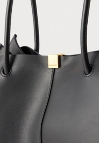 Borsa in pelle nera con due manici arrotondati e una piccola fibbia quadrata dorata con la scritta "COCCINELLE" al centro in alto.