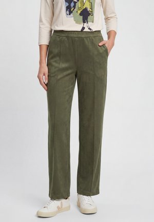 Donna che indossa pantaloni dritti verde oliva con tasche laterali e sneakers bianche, mostrata da metà torso ai piedi.
