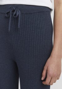 Navy ribbed trousers made of soft fabric, featuring a drawstring waist and textured surface with vertical lines for added detail.