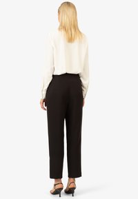 Schwarze hochtaillierte Hosen mit geradem Bein, kombiniert mit einer weißen Bluse mit langen Ärmeln. Hat eine glatte Textur und ein minimales Design.