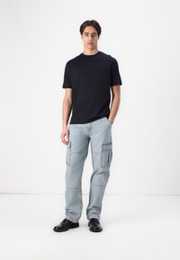 Jūrų mėlynos spalvos crewneck marškinėliai derinami su šviesiai mėlynomis cargo kelnėmis, turinčiomis kelis kišenes, užbaigta juodais raišteliais bateliais. Minimalistinis dizainas.