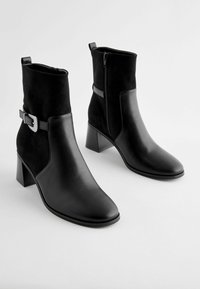 Bottines noires en cuir et daim, dotées d'un bout carré, d'un talon bloc, d'une fermeture éclair sur le côté et d'un accent de boucle décoratif.
