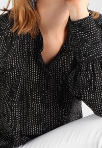 Camicia nera con strisce verticali bianche, caratterizzata da un design con bottoni, maniche a risvolto e un tessuto morbido e testurizzato.
