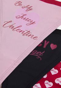 Trīs sieviešu apakšveļas komplekti: rozā ar uzrakstu "Be My Juicy Valentine", melns ar "Juicy Angel" un sarkans ar sirds rakstiem.