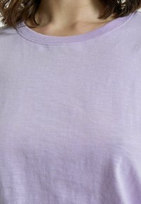 Svetlofialová bavlnená tričko s okrúhlym výstrihom a krátkymi rukávmi. Hladká štruktúra so subtílnymi variáciami v farbe a tkaní.