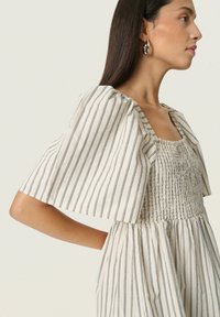 Lightweight, striped dress in cream and navy with a square neckline, smocked bodice, and flutter sleeves. Smooth texture and flowy silhouette.