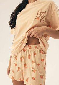 Zestaw piżamowy w kolorze brzoskwiniowym z bawełny, składający się z krótkiego topu z nadrukiem "C'est la Vie" oraz spodenek w brzoskwiniowy wzór. Gładka, miękka tekstura.