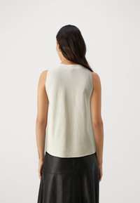 Light green sleeveless knit top with a textured back, featuring a rounded neckline and an asymmetric hem, paired with a black leather skirt.