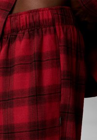 Zone de la taille d’un pantalon à taille élastique à carreaux rouges et noirs porté par une personne à la peau foncée.