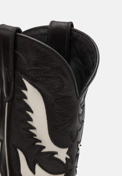 Schwarz-weißer Leder-Cowboystiefel mit flammen- und blattähnlichen gestickten Mustern am oberen Teil vor weißem Hintergrund.