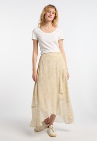 Lys gul, svævende maxi-nederdel med en asymmetrisk kant og cirkulært mønster. Bæres med en almindelig hvid top og beige sneakers.