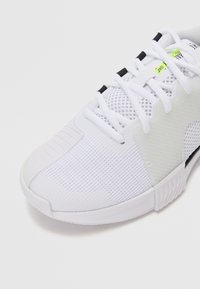 Weißer Sportschuh mit Mesh-Obermaterial, Gummisohle und schwarzen Akzenten. Verfügt über ein Schnürdesign und strukturierte Einsätze zur Belüftung.