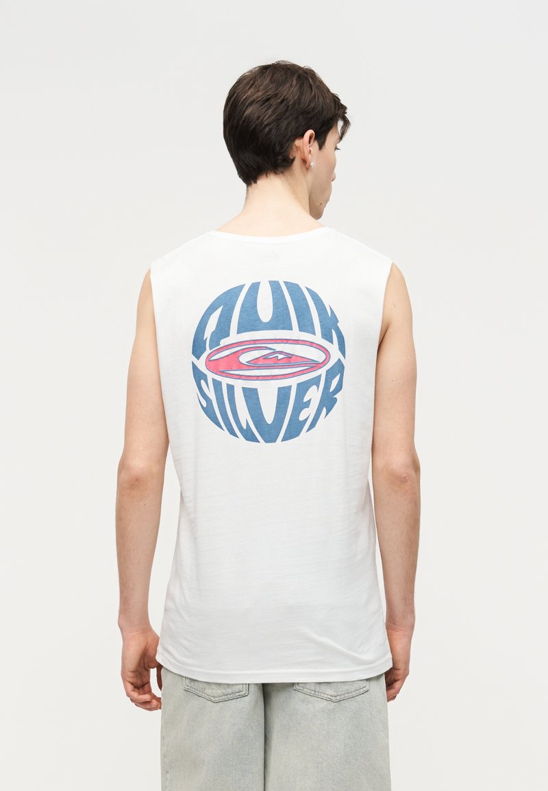 Noor mees, kes on seljaga vaatajast eemale pööratud, kannab valget varrukateta särki, millel on suur sinine ja punane Quiksilveri logo seljal.