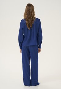 Set di blusa blu e pantaloni a gamba larga realizzati in tessuto morbido. La blusa presenta una vestibilità ampia e maniche lunghe; i pantaloni hanno una silhouette rilassata.