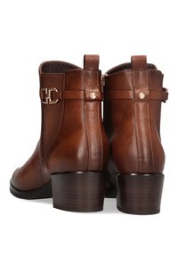 Botas de tobillo de cuero marrón con punta redondeada, tacón bajo tipo bloque, detalle de hebilla lateral y costuras tonales a lo largo de las costuras y paneles.