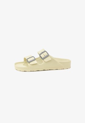 Sandalo a ciabatta color crema con due cinturini regolabili e fibbie argentate, suola piatta e fondo testurizzato per una migliore aderenza.