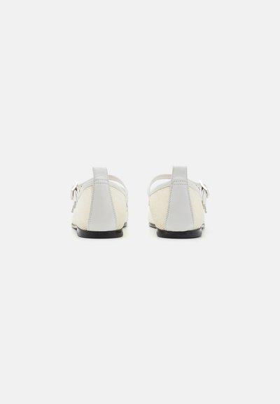 Chaussures en cuir blanc avec un avant en tissu beige texturé, languette arrière pour un enfilage facile et semelles en caoutchouc noir. Pas de matériel ou d'accents supplémentaires.