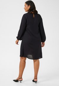 Vestido negro de longitud hasta la rodilla con mangas largas abullonadas y un abertura en la espalda en forma de llave. Textura suave, tela ligera y acabado ligeramente transparente.