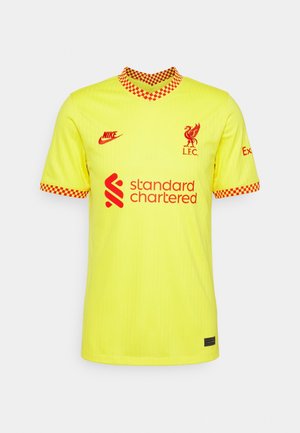 Žlutý fotbalový dres Liverpoolu s červeným kostkovaným límcem a lemováním rukávů, červeným logem Nike, klubovým znakem a nápisem sponzora Standard Chartered.