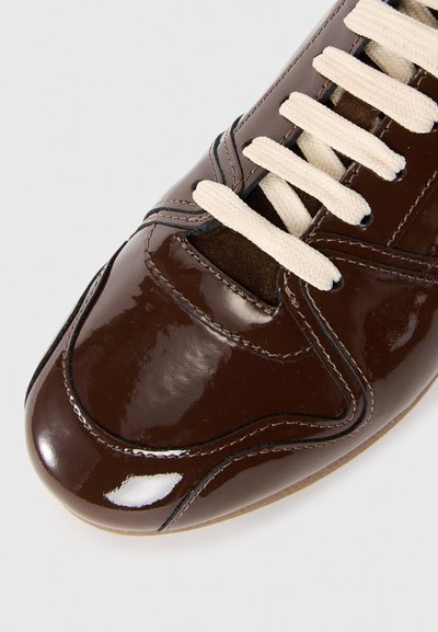 Brun lackläder sneaker med krämfärgad snörning, med rund tå och sydda detaljer längs ovansidan för ökad stil.