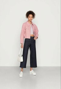 Casaco cropped rosa claro, top cropped às riscas, jeans largos escuros, ténis brancos e uma pequena bolsa branca, com um design clássico.