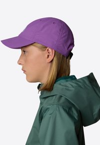 Cappellino da baseball viola con visiera curva, dotato di dettagli cuciti e di una striscia nera regolabile sul retro. Indossato con una giacca con cappuccio verde.