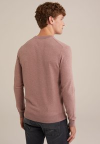 Suéter de punto rosa claro con mangas largas, escote redondo y puños y dobladillo acanalados. Modelo visto desde la espalda, vistiendo pantalones gris oscuro.