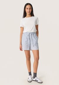 T-shirt courte à manches blanches et shorts à rayures bleues avec taille élastique. Associé à des chaussettes grises et des baskets blanches avec des rayures noires.