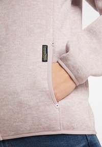 Felpa a maglia rosa chiaro con finitura testurizzata, dotata di una tasca laterale bordata in un tessuto a contrasto e di un'etichetta con logo cucita sulla cucitura.