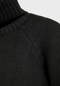 Maglione nero a collo alto in maglia, che mostra una texture dettagliata e un colletto a coste, con focus sulla zona spalla e collo.