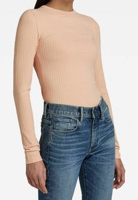 Top z długim rękawem w prążkowanym wzorze, w delikatnym brzoskwiniowym kolorze, z okrągłym dekoltem, zestawiony z jasnoniebieskimi dopasowanymi jeansami o klasycznej teksturze denimu.