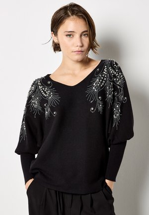 Czarny sweter dziergany z dekoltem w kształcie litery V, bufkami na rękawach oraz skomplikowanym zdobieniem koralikami na ramionach. Miękka tekstura i luźny krój.