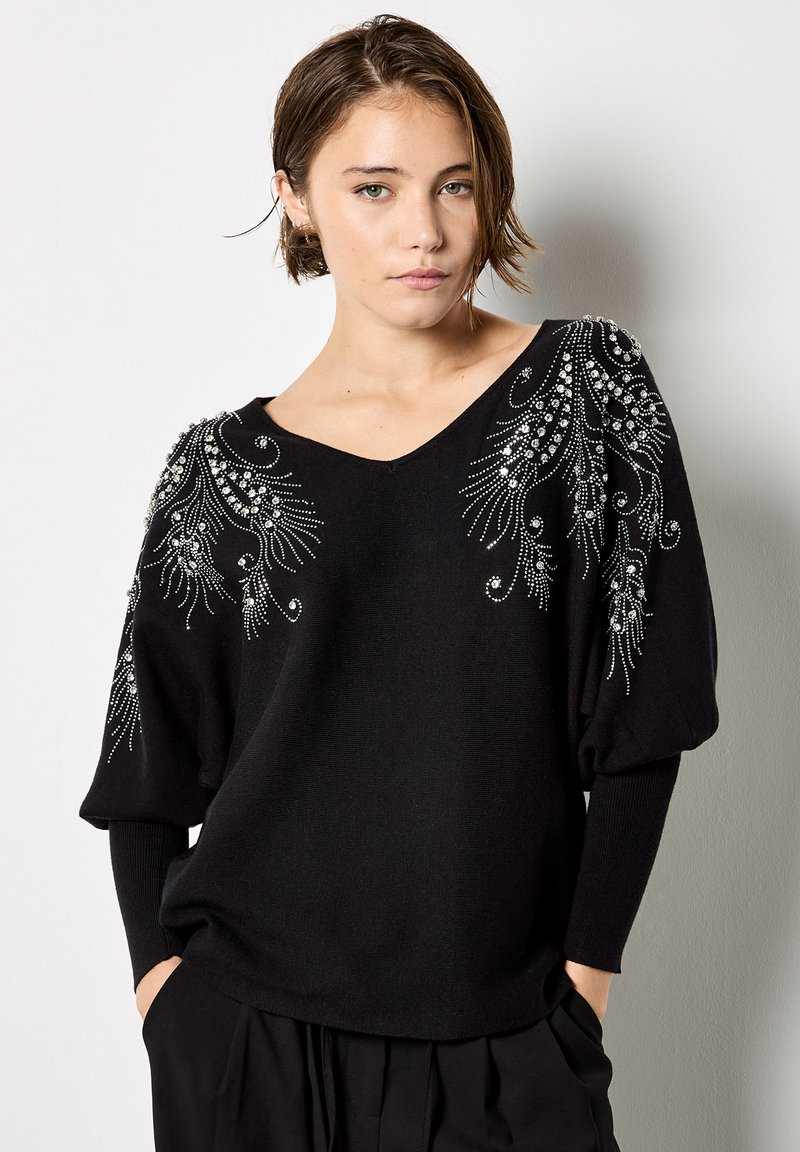 Czarny sweter dziergany z dekoltem w kształcie litery V, bufkami na rękawach oraz skomplikowanym zdobieniem koralikami na ramionach. Miękka tekstura i luźny krój.