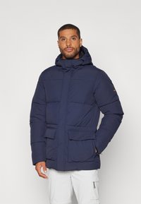 Mørkeblå puff-jakke med hette, med frontglidelås, to store klaftlommer og polstrede seksjoner for isolasjon.