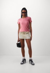 Rosa geripptes Kurzarmoberteil mit gewellten Kanten, kombiniert mit einem hellbeigen Denim-Minirock, einer schwarzen Handtasche und schwarz-weißen Sneakers.
