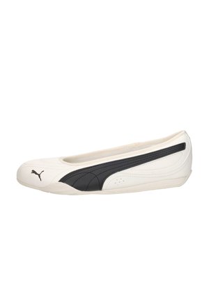 Zapato plano blanco Puma con perfil bajo, superficie lisa y una franja negra con el logo de Puma a lo largo del lateral y la puntera.