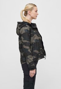 Camouflage jacket in tones of green and black, featuring a hood, front zip, and side pockets. Material appears smooth and weather-resistant.
