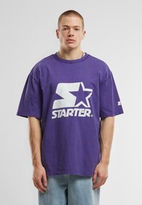 T-shirt violet surdimensionné en coton, arborant un grand logo blanc "Starter" avec un design d'étoile. Col rond et manches courtes.