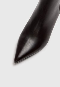 Zapato de cuero negro con puntera afilada, de textura suave y diseño elegante, con una punta larga y sin hardware visible.