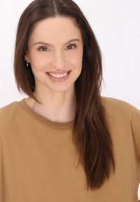 Ritratto di una persona con lunghi capelli castani, che indossa un maglione marrone chiaro a girocollo. Lo sfondo è bianco puro. Illuminazione soffusa.