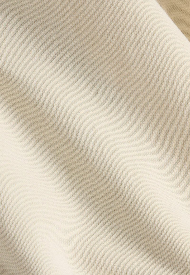 Weicher cremiger Stoff mit feiner, strukturierter Webart. Leicht gespannt, zeigt er sanfte, subtile Farb- und Tiefenvariationen.