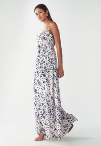 Robe maxi en tissu léger, rose pâle à pois bleu marine, bretelles spaghetti ajustables et détail à nouer à la taille. Fente sur le côté.