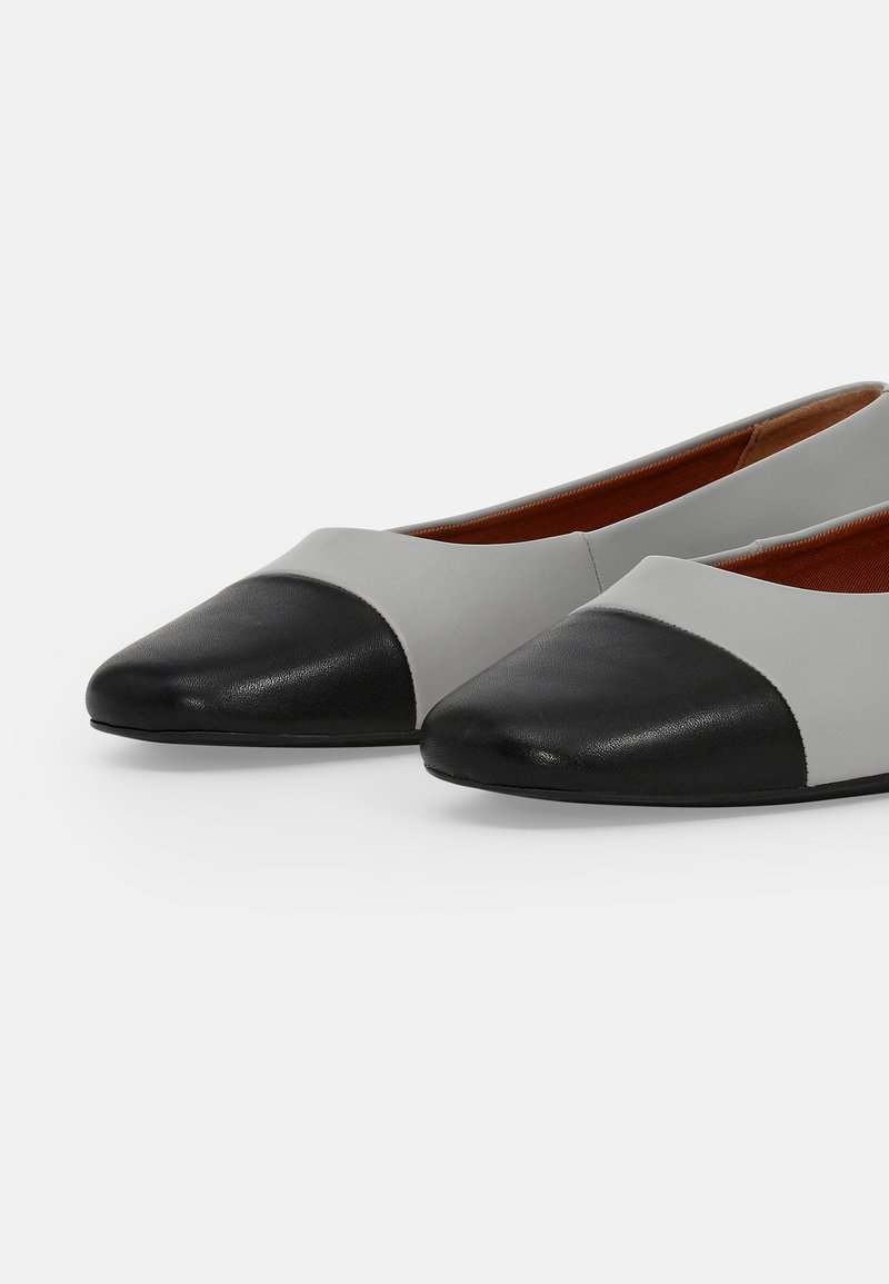 Baleriny z rozdzielonym fasonem w szarej skórze z czarnym okrągłym noskiem. Wnętrze ma brązowe wykończenie, co tworzy kontrast kolorów.
